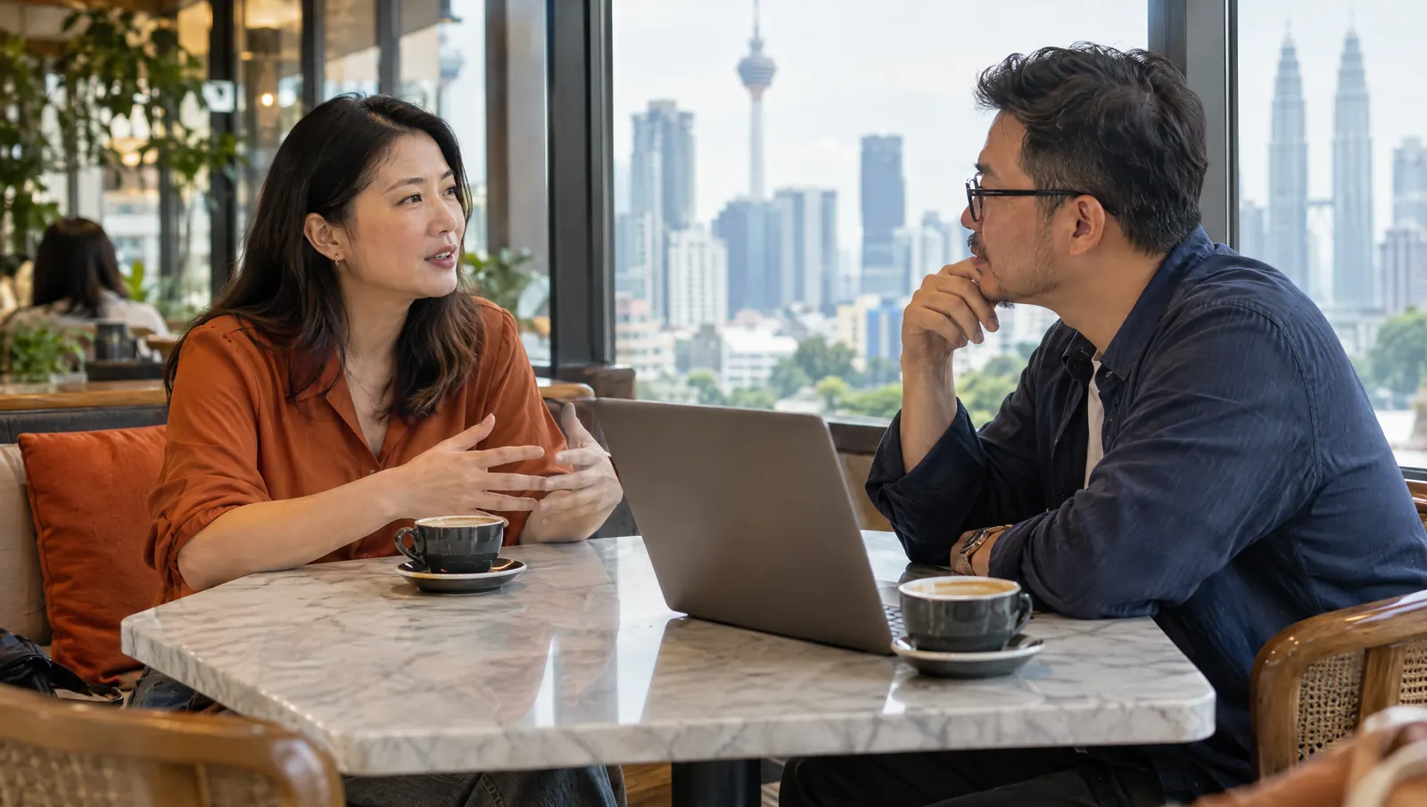 Pemilik perniagaan Malaysia berjumpa web designer di kafe dengan pemandangan Kuala Lumpur di luar